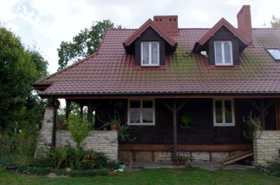 Drewniany dom z czerwoną dachówką na tle ogrodu.